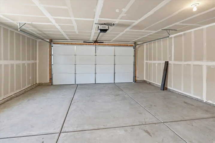 Concrete flooring, white overhead garage door, built-in overhead garage door opener, recessed lighting, and unpainted drywall