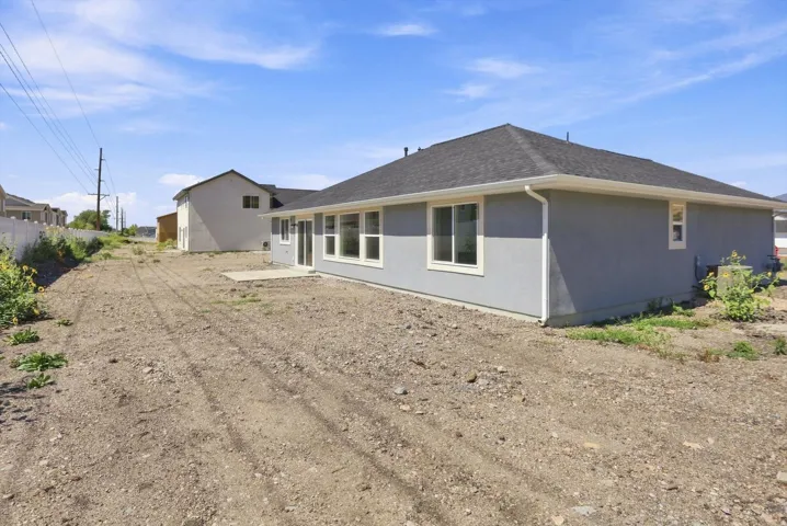 Stucco exterior with a dark shingle roof, multiple windows, and a concrete patio