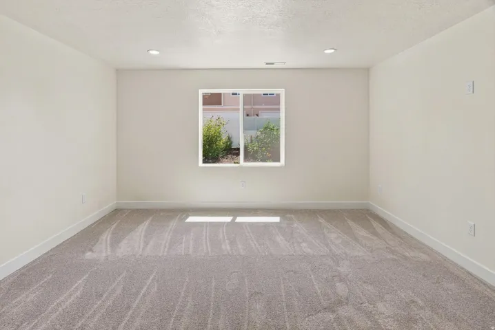 Recessed lighting illuminates neutral walls and gray carpet flooring, complemented by a white-trimmed window
