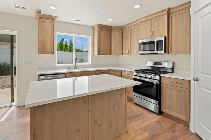 Wood-finish flooring, central island with light-toned countertop, stainless steel appliances, light wood-tone cabinetry, and recessed lighting