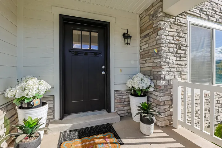 Craftsman-style entry door with glass paneling, durable siding exterior, stone facade accents, exterior wall sconce, and white porch railing