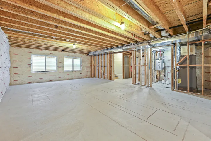 Unfinished basement featuring exposed wood joists, concrete flooring, and multiple window openings