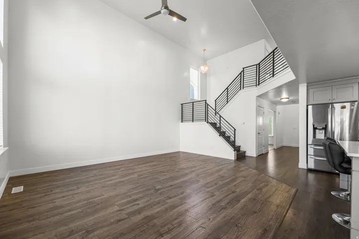 Vaulted ceilings, wood-finish flooring, staircase with modern metal railing, recessed lighting, and stainless steel refrigerator