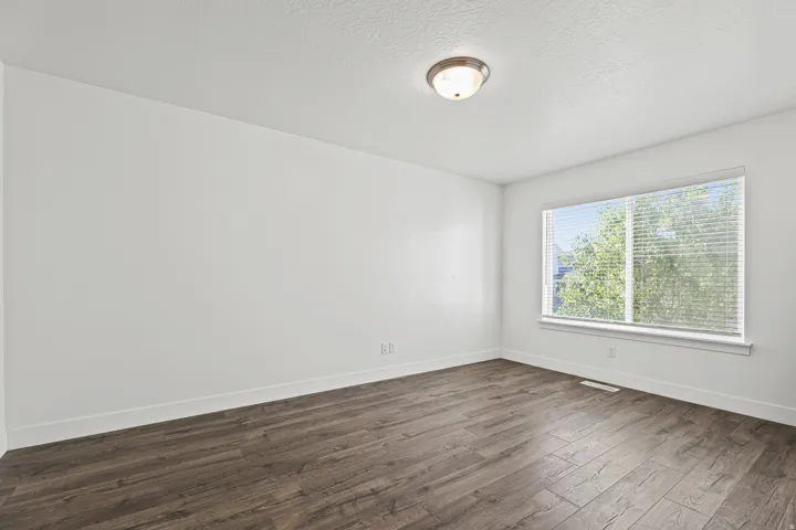 Spacious room featuring wood-finish flooring, a large window with blinds, and an overhead flush-mount light fixture