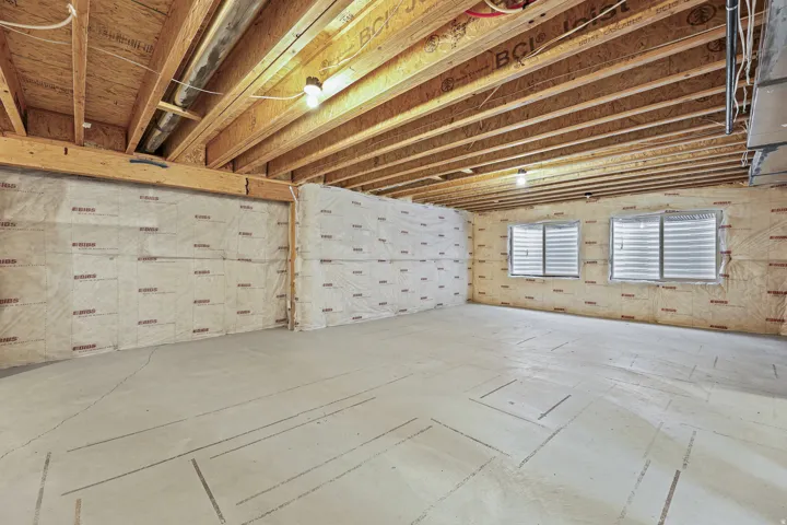 Unfinished lower level featuring exposed wood joists, insulated exterior walls, concrete flooring, and two window wells