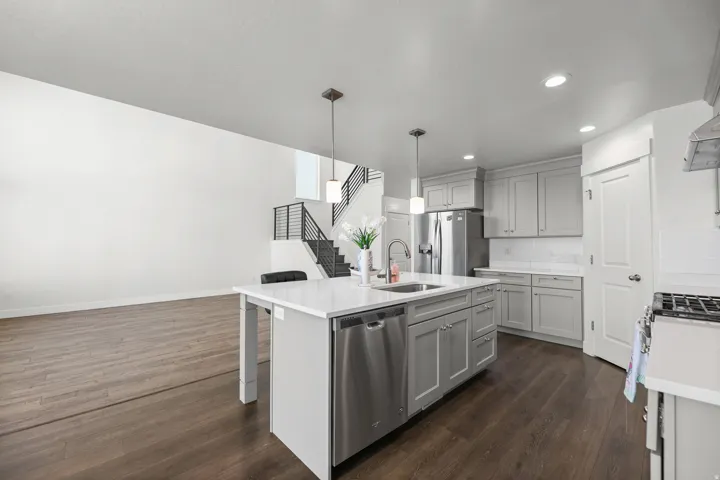 Spacious kitchen featuring an island with a built-in sink and pendant lighting, stainless steel appliances, light gray cabinetry, and wood-finish flooring