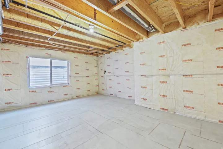 Unfinished lower level featuring exposed ceiling joists, insulation-wrapped walls, and a concrete floor