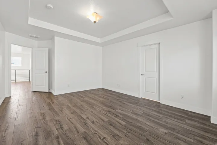 Room featuring wood-finish flooring, white walls, a tray ceiling, and a flush mount light fixture