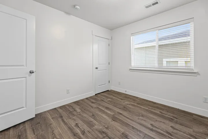 Wood-finish flooring, white paneled doors, and a window with blinds