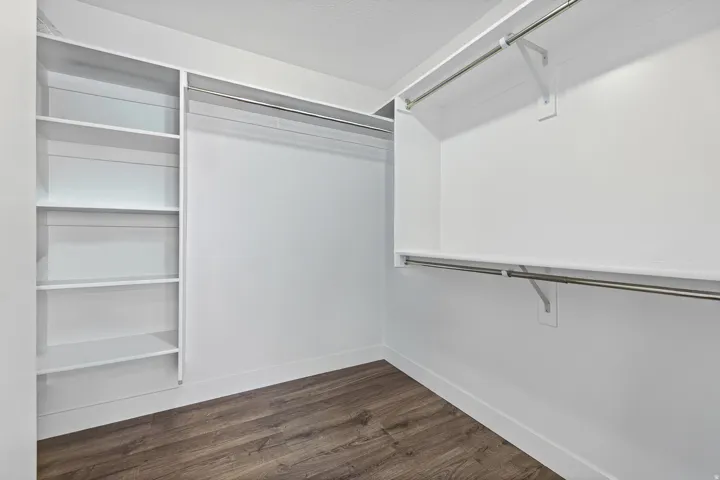 Master  walk-in closet - Custom built-in shelving, dual clothing rods, wood-finish flooring, and white painted walls