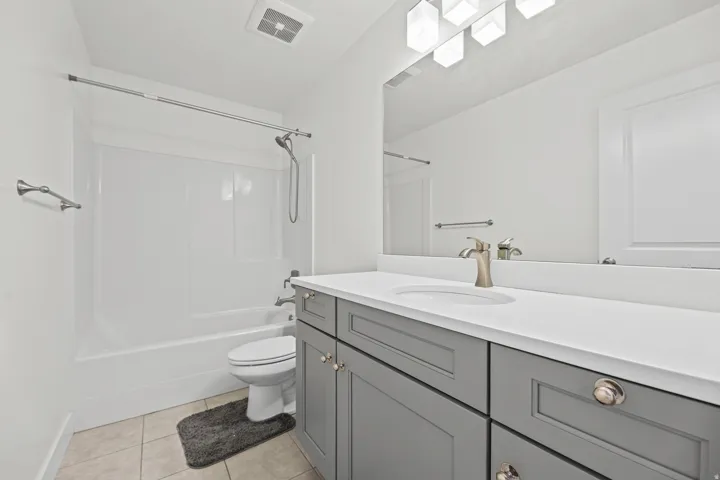 Bathroom featuring a white tub/shower combination, gray vanity with brushed nickel hardware, and tile flooring