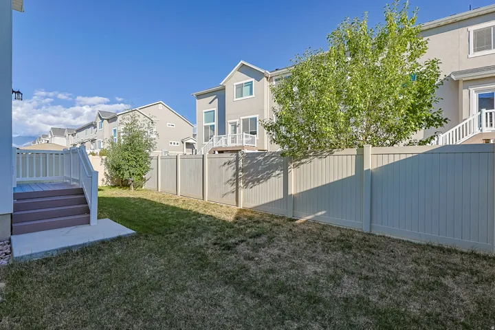 Grass lawn, white privacy fencing, deck with white railing, and exterior wall-mounted lighting