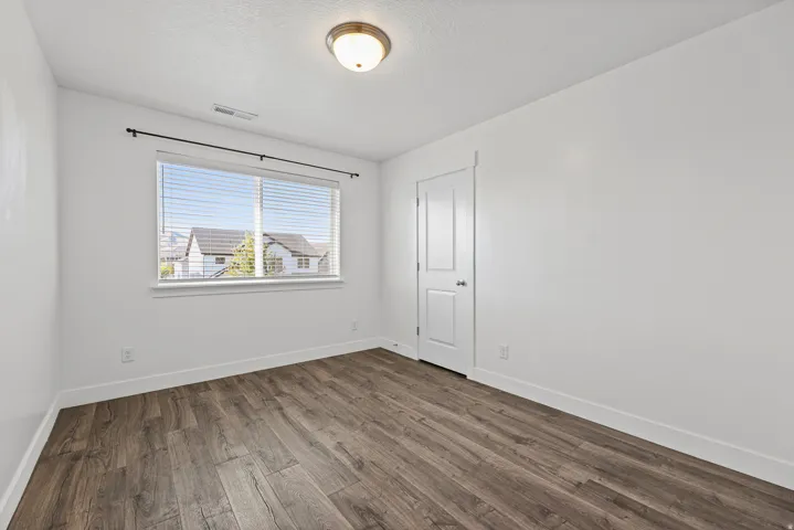 Wood-finish flooring, crisp white walls, and a recessed window with horizontal blinds