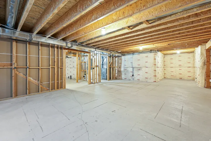 Unfinished basement with exposed wood joists, concrete flooring, and framed interior walls