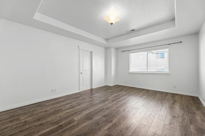 Tray ceiling with recessed lighting, wood-finish flooring, and a large window with blinds
