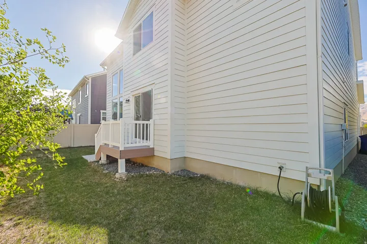 White siding exterior with a ground-level patio, an elevated deck with white railings, and a sliding glass door