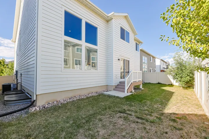 White siding exterior with multiple large windows, a ground-level patio, and a privacy fence