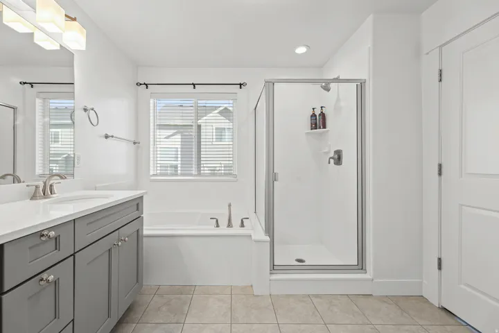 Dual vanity with brushed nickel hardware, contemporary light fixture, built-in soaking tub, separate glass-enclosed shower, and tiled flooring