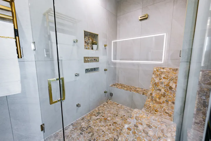 Glass-enclosed shower with pebble-finish flooring and integrated bench seating