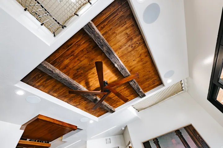 Exposed wood plank ceiling with rustic beams, integrated ceiling fan, recessed lighting, and built-in ceiling speakers
