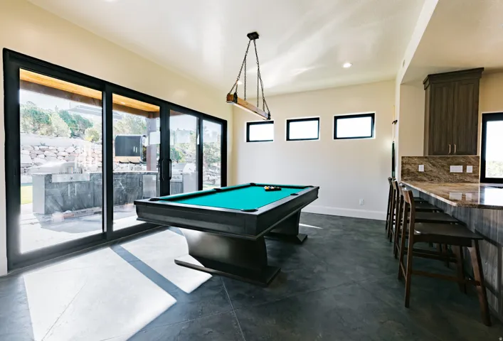 Expansive sliding glass doors, dark flooring, built-in bar with stone countertop, and custom cabinetry
