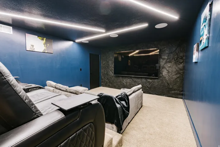 Integrated ceiling lighting, recessed ceiling speakers, textured accent wall, dark painted ceiling, wall-mounted television