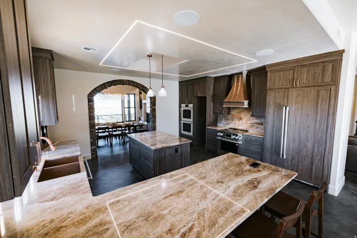 Kitchen featuring custom cabinetry, integrated appliances, two large islands with stone countertops, and an arched stone entry