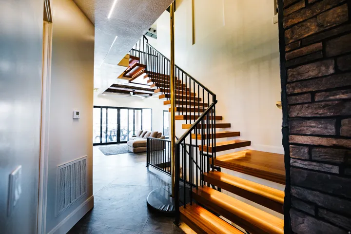Open staircase with wood-finish treads, black metal railings, and a central brass-finish support