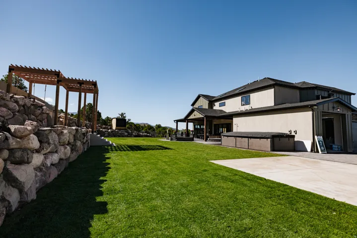 Expansive rear yard featuring a large turf area, stone retaining wall, and a wood pergola