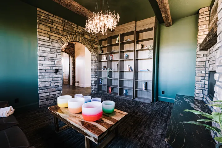 Stone archway entrance, built-in shelving, exposed wood ceiling beams, stone fireplace with a dark stone hearth, and textured flooring