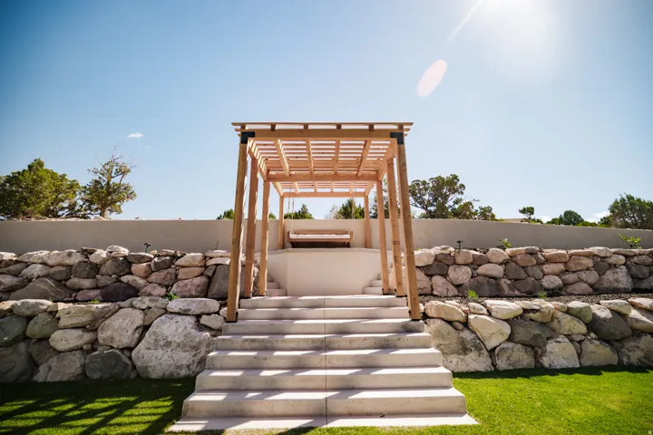 Manicured lawn with concrete steps leading to a wooden pergola and a stone retaining wall