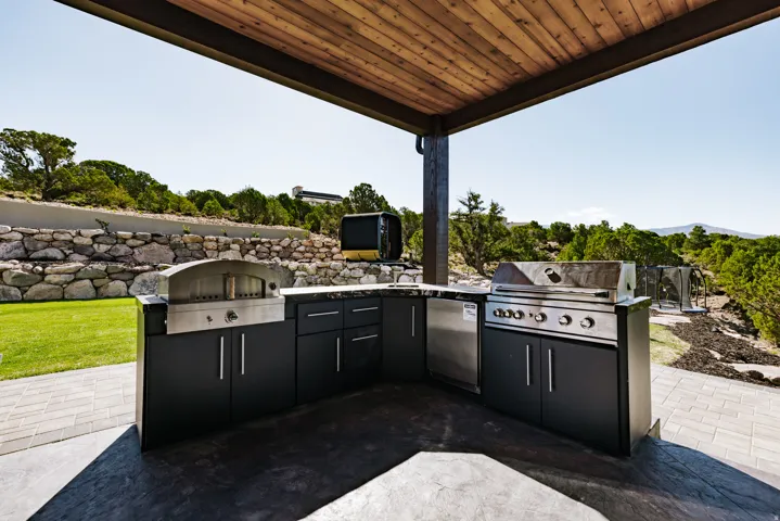 Covered outdoor kitchen featuring a built-in grill, pizza oven, and integrated refrigerator