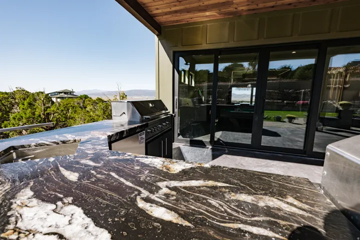 Outdoor kitchen featuring a built-in stainless steel grill, integrated sink, and patterned stone countertops