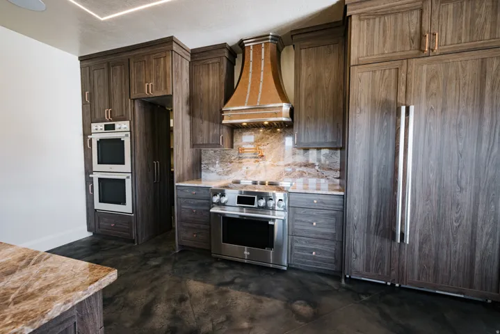 Gourmet kitchen featuring wood-finish cabinetry, stainless steel appliances, a custom range hood, stone countertops, and a full-height stone backsplash