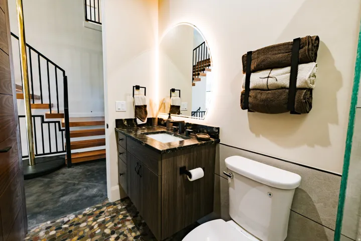 Modern vanity with a dark countertop and integrated sink, illuminated mirror, and pebble-finish flooring