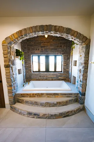 Stone-clad archway featuring a built-in soaking tub, a multi-pane window, and recessed shelving