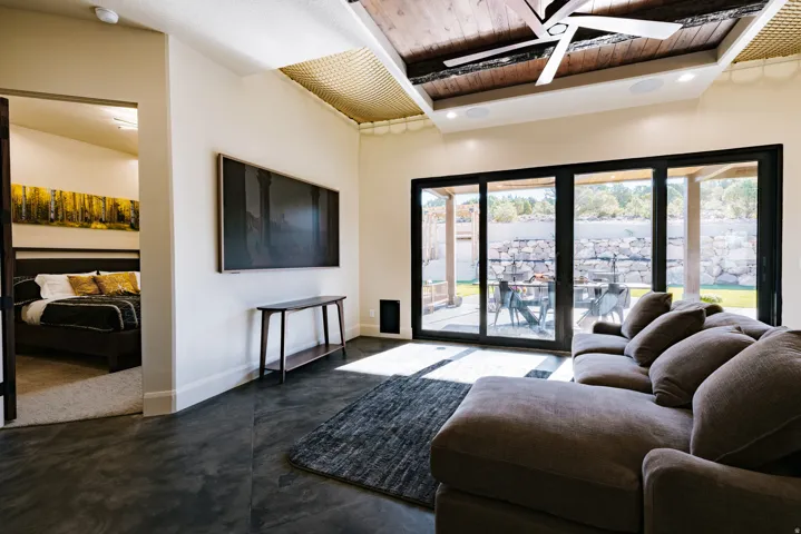 Vaulted ceiling with wood-paneled beams, dark-toned flooring, and expansive multi-panel sliding glass doors
