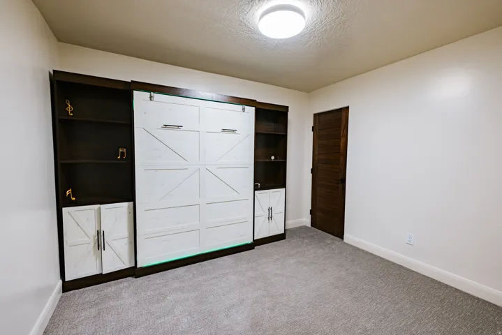 Built-in cabinetry with open shelving and closed storage, integrated Murphy bed, textured ceiling, and a dark wood-finish interior door
