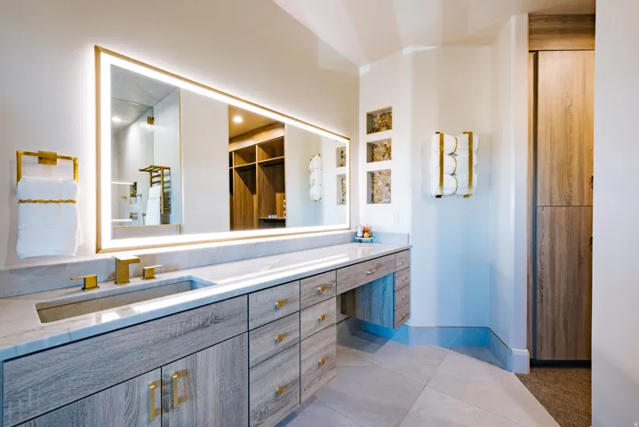Integrated vanity with a single basin, light wood-finish cabinetry, and gold-finish hardware