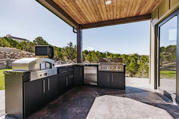 Covered patio with a wood-plank ceiling, built-in outdoor kitchen with stainless steel appliances, and a glass-paneled exterior door