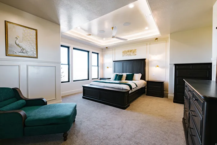 Tray ceiling with recessed lighting and a ceiling fan, wall paneling, multiple windows with dark frames, and carpeted flooring