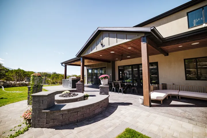 Expansive paver patio with a built-in fire pit, covered outdoor living space, wood-finish ceiling, and stucco exterior