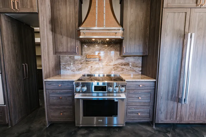 Stainless steel range, custom range hood, stone backsplash, granite countertops, and wood-finish cabinetry