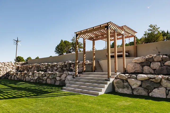 Expansive terraced yard featuring natural stone retaining walls, a wooden pergola, concrete steps, and a lush lawn