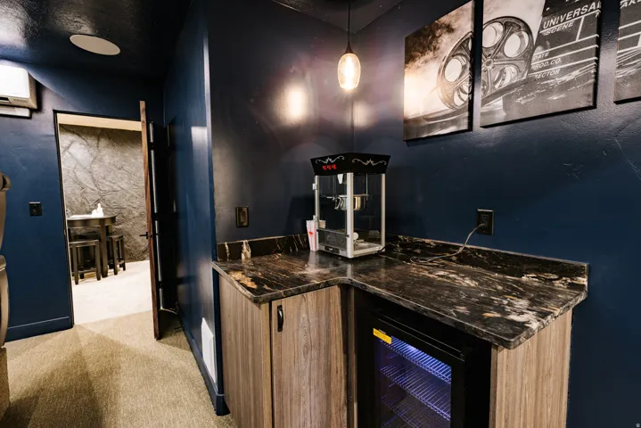 Built-in wet bar with a compact refrigerator, wood-finish cabinetry, and a dark stone-finish countertop