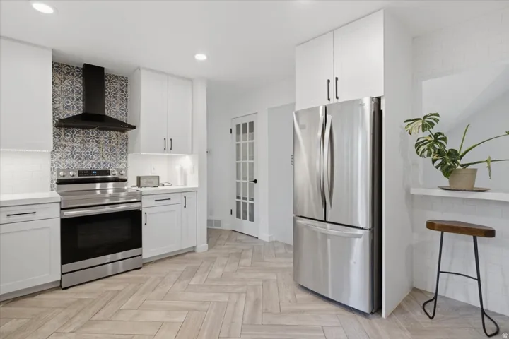 Stainless steel appliances, white cabinetry, herringbone-pattern wood-finish flooring, patterned tile backsplash, and recessed lighting