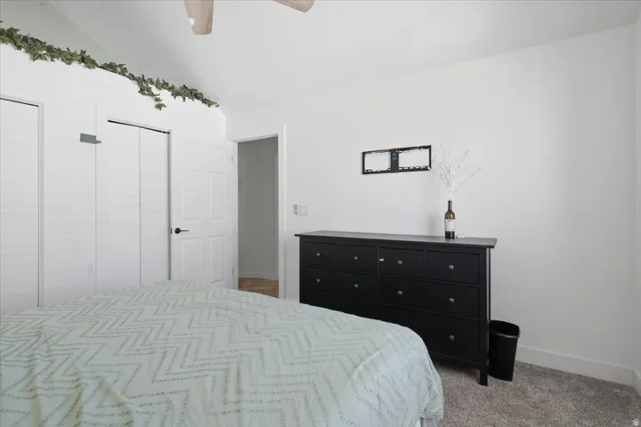Vaulted ceiling, two louvered closet doors, wall-mounted light fixture, carpeted flooring, and white wall finishes