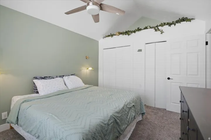 Vaulted ceiling, ceiling fan, wall-mounted light fixtures, two bi-fold closet doors, and a paneled interior door