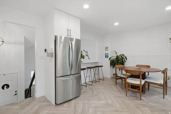 Stainless steel French door refrigerator, white upper cabinetry, recessed lighting, accent wall paneling, and wood-finish flooring in a herringbone pattern