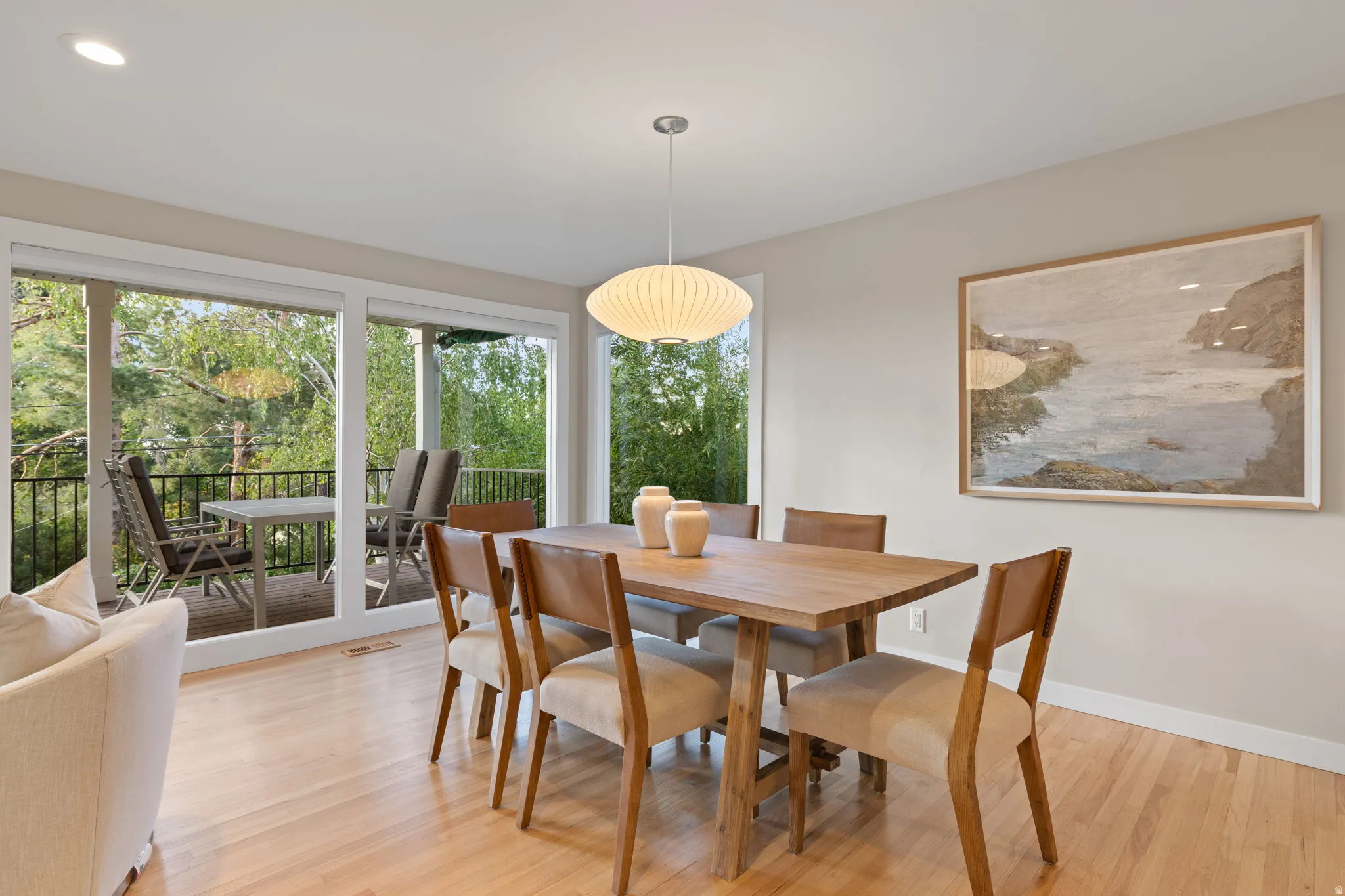 Dining area with Herman Miller light fixture, hardwood flooring and floor to ceiling windows facing the backyard landscape